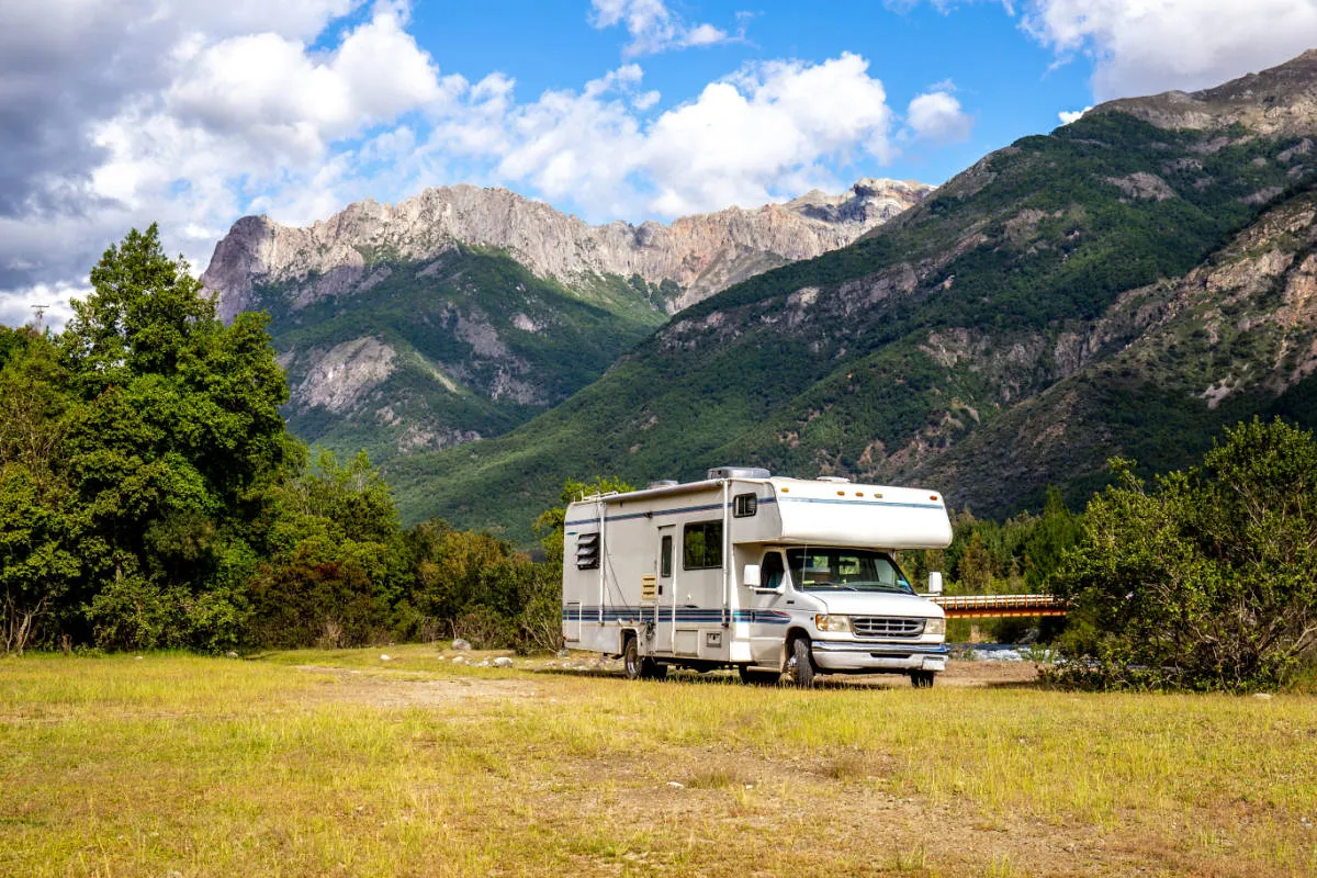A Class C motorhome camped off-grid in a green mountain valley, the kind of RV trip CampVerdict helps you power, rent and park