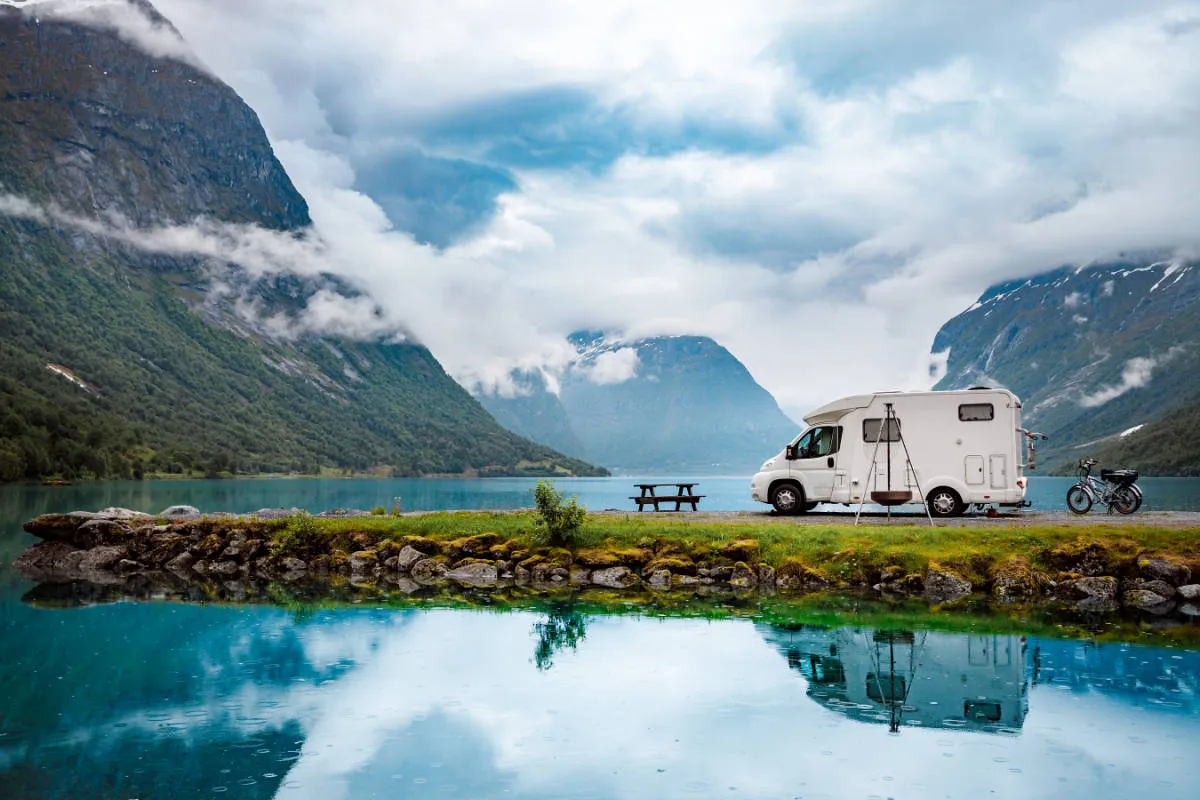 A Class C motorhome parked by a mountain lake, the RV type our rental cost guide prices at about $230 a night