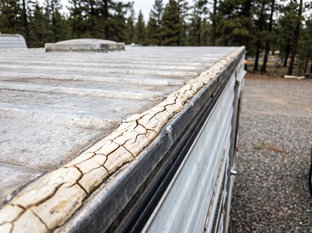 Cracked and yellowed sealant running along the edge trim of a camper roof seam.