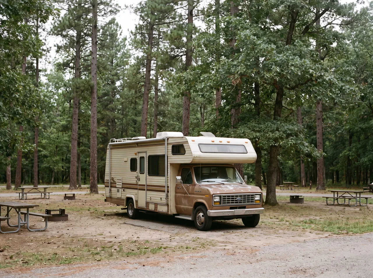 A small motorhome with an over cab bunk parked at a rural campground.