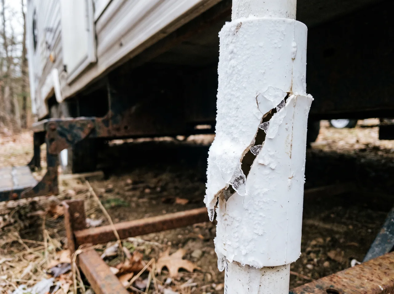 A water line under a camper split open along its length by ice, the insulation torn back and frost still on the pipe.