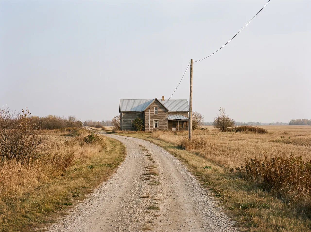 A rural house set far back from a gravel road, a single utility pole carrying the line toward it.