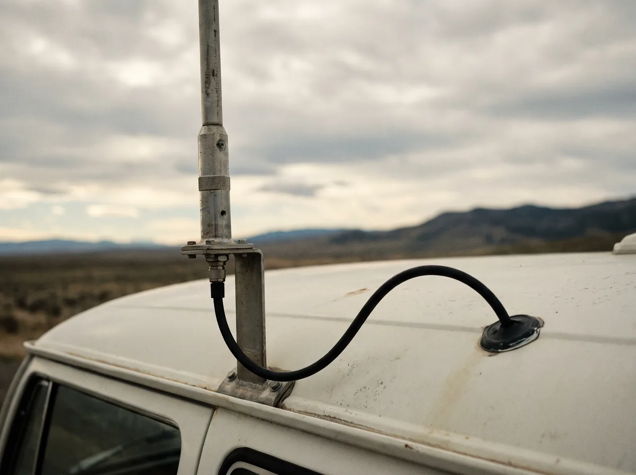 An antenna mast mounted on the roof of a camper with its cable running into a deck fitting, open country behind.