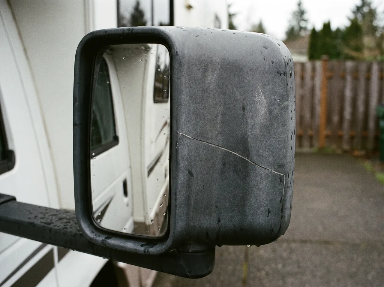 The side mirror of a motorhome in close focus, a scratch running across the housing.