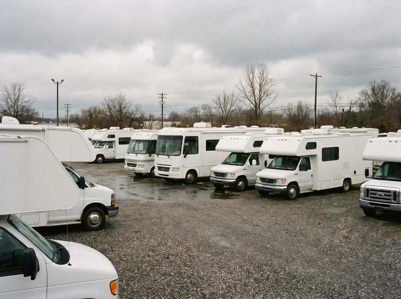 Motorhomes of varying sizes parked side by side in a rental lot under overcast light.